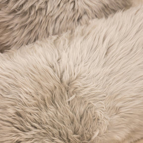 Close-up texture of New Zealand sheepskin cushion in pale grey showing soft dense long wool fibres