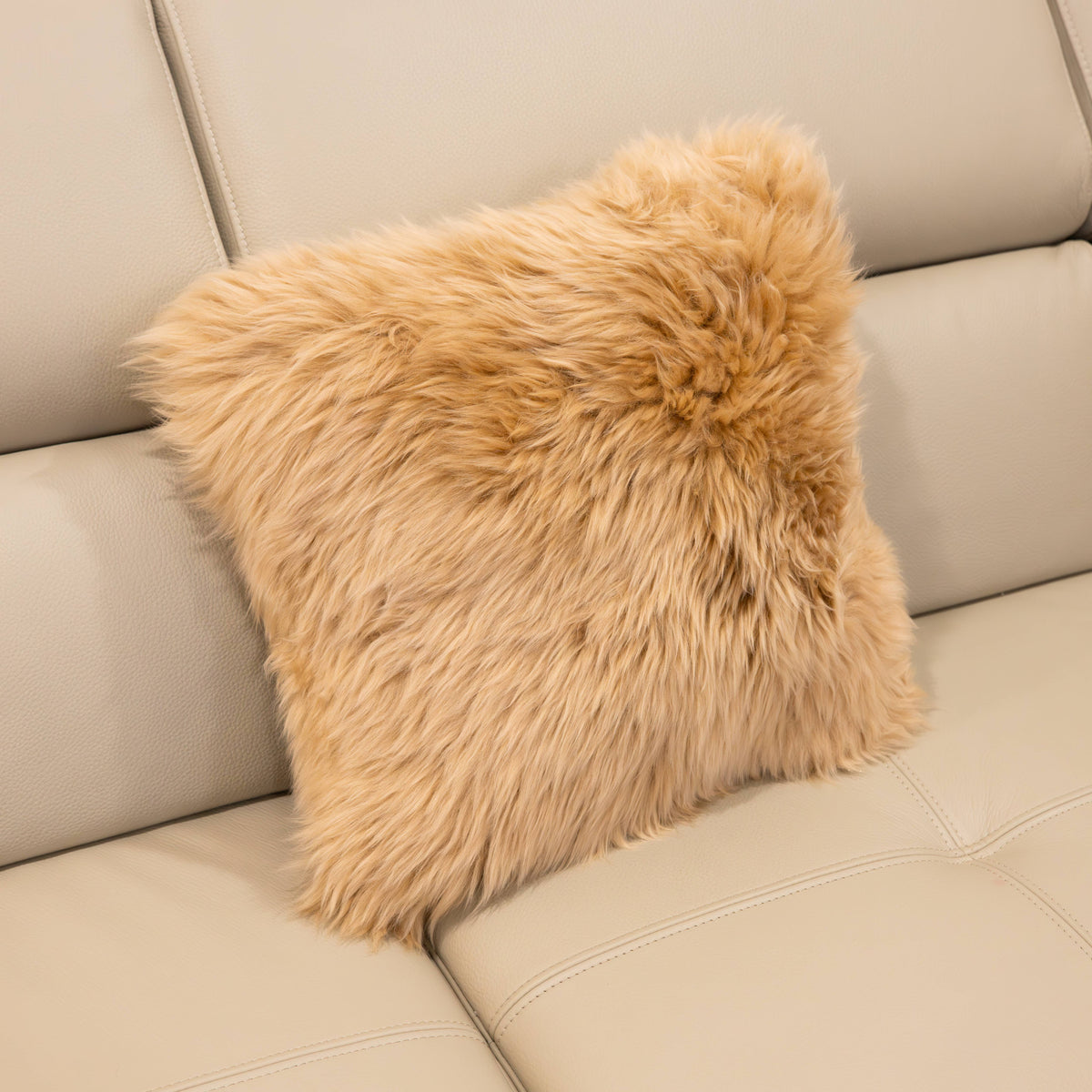New Zealand sheepskin cushion in sand with soft long wool texture displayed on a beige sofa