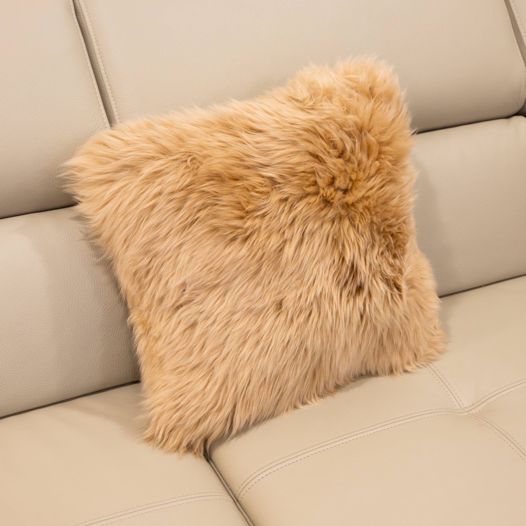 New Zealand sheepskin cushion in sand with soft long wool texture displayed on a beige sofa
