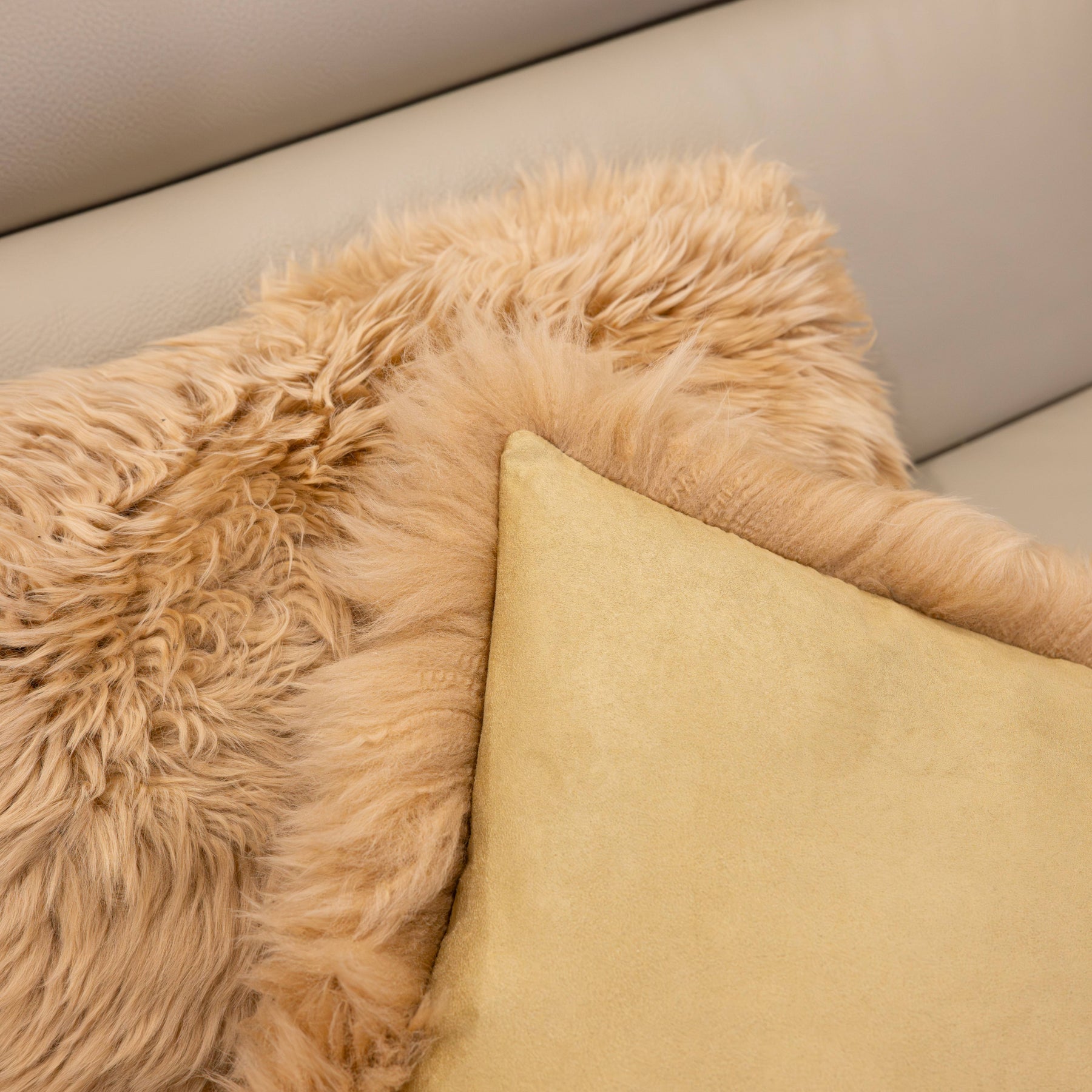 Close-up of New Zealand sheepskin cushion in sand showing plush long wool front and soft backing fabric detail