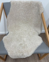 Oatmeal shearling rug draped over a chair featuring soft tightly curled wool.