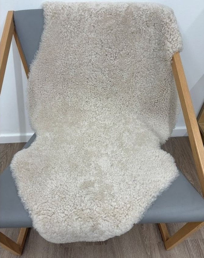 Oatmeal shearling rug draped over a chair featuring soft tightly curled wool.