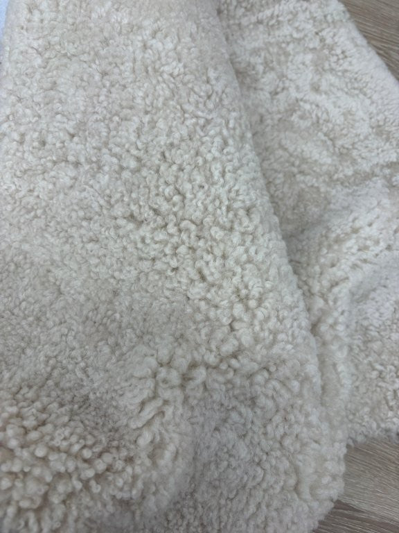 Detailed view of genuine oatmeal shearling with soft, tightly curled wool fibres.