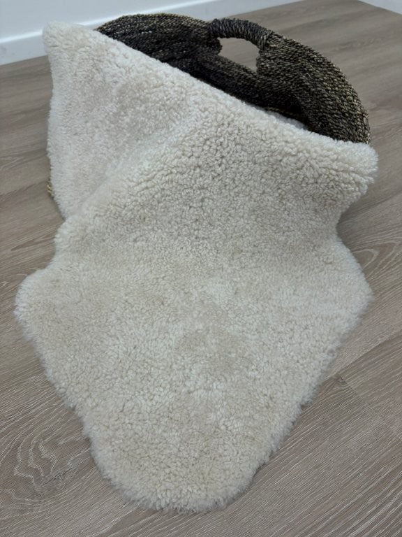 Genuine oatmeal shearling sheepskin rug showcasing its natural hide shape and dense curly wool.