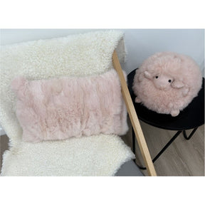 Soft pink rabbit fur lumbar cushion styled on chair with shearling throw