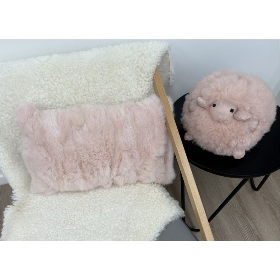 Soft pink rabbit fur lumbar cushion styled on chair with shearling throw