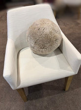 Shearling accent ball in bone colour styled on a white armchair, showcasing its round sculptural form and soft textured shearling finish