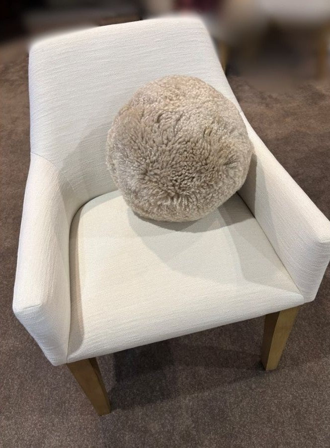 Shearling accent ball in bone colour styled on a white armchair, showcasing its round sculptural form and soft textured shearling finish