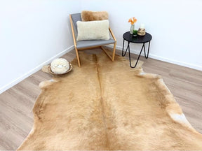 Solid beige cowhide rug styled in a living space with a chair, cushion and side table on a timber floor