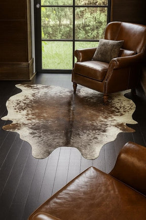Speckled longhorn cowhide rug small size genuine hide with natural markings styled in interior space with leather armchair on timber floor