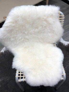 Icelandic shorn sheepskin rug in natural white draped over a woven chair as a styling accent