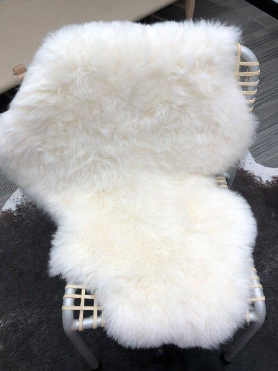 Icelandic shorn sheepskin rug in natural white draped over a woven chair as a styling accent
