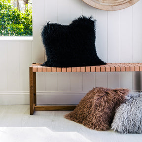 Black Mongolian sheepskin cushion with long hair texture styled on a wooden bench in a neutral interior