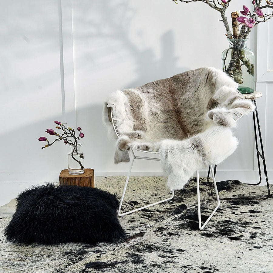 Black Mongolian sheepskin cushion with long hair texture styled on the floor beside an accent chair in a living space