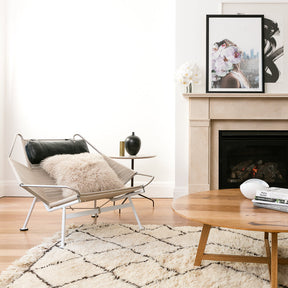 Fawn Mongolian sheepskin cushion styled on a modern chair in a living room with fireplace and neutral décor