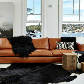 Brown and black Icelandic sheepskin rug styled on the floor beside a leather sofa in a modern living space