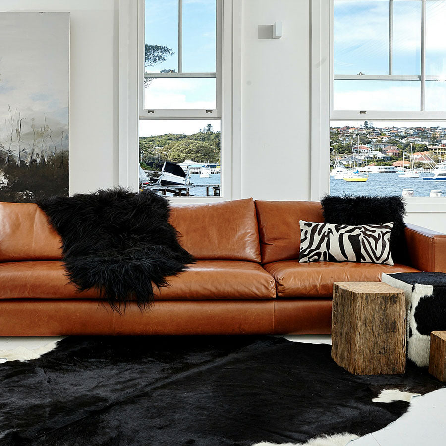 Brown and black Icelandic sheepskin rug styled on the floor beside a leather sofa in a modern living space