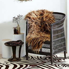 Icelandic sheepskin rug in copper with caramel tips draped over a woven chair in a living space