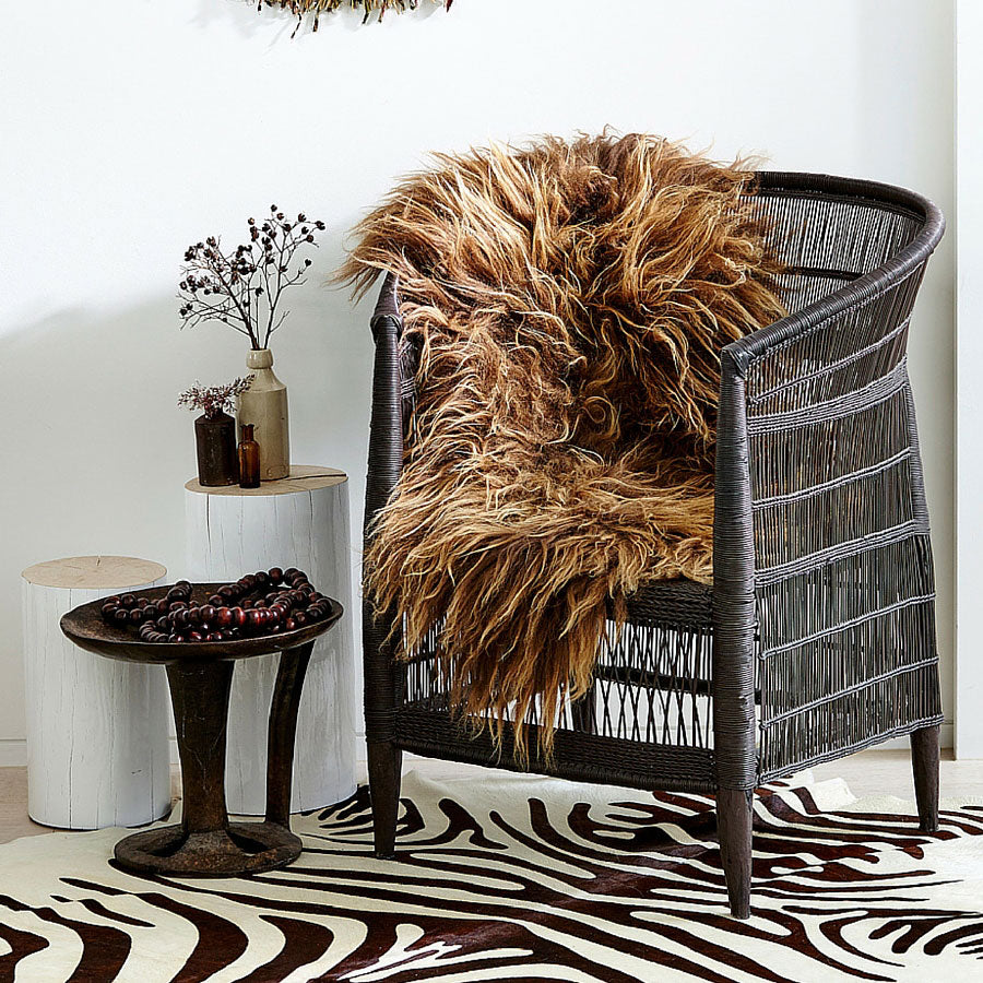 Icelandic sheepskin rug in copper with caramel tips draped over a woven chair in a living space