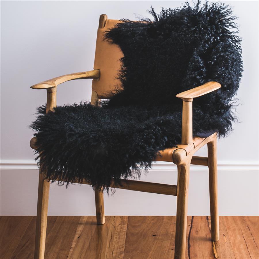 Black Mongolian sheepskin rug styled over a wooden chair in a minimalist interior