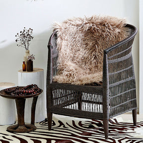 Camel Mongolian sheepskin rug styled over a wicker chair in a warm, styled living space