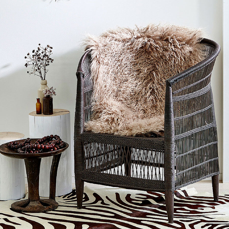 Camel Mongolian sheepskin rug styled over a wicker chair in a warm, styled living space