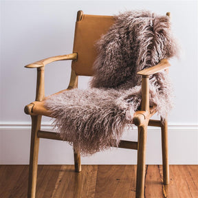 Camel Mongolian sheepskin rug styled over a wooden chair in a warm, neutral interior
