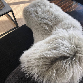 Grey Mongolian sheepskin rug with white tips draped over a chair in a styled interior