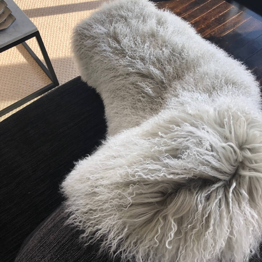 Grey Mongolian sheepskin rug with white tips draped over a chair in a styled interior