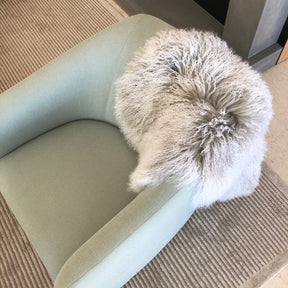 Grey Mongolian sheepskin rug with white tips styled over a modern armchair