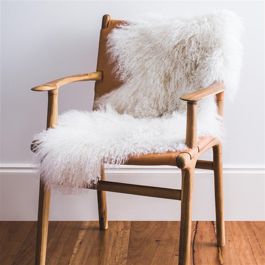 atural white Mongolian sheepskin rug styled over a wooden chair in a minimalist interior