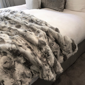 White and grey rabbit hide blanket draped over a bed showing natural hair texture and colour variation