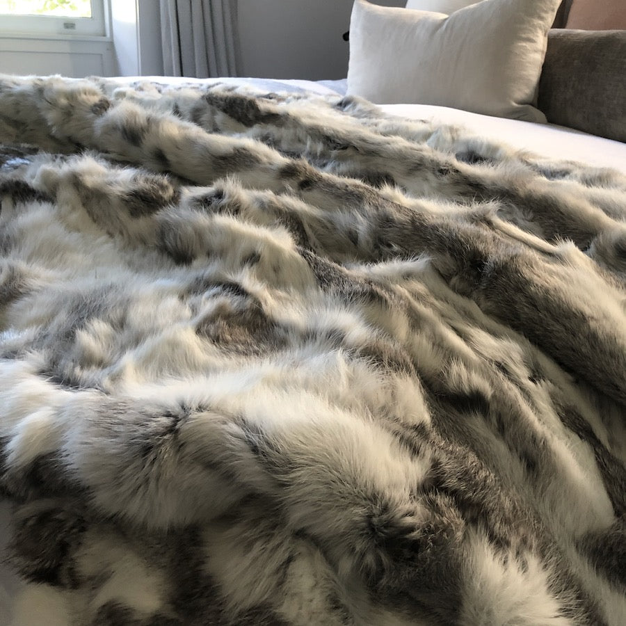 White and grey rabbit hide blanket styled across a bed showing soft natural hair texture