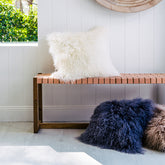 White Mongolian sheepskin cushion with long hair texture styled on a wooden bench in a light, modern interior