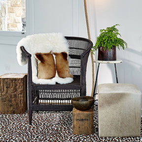 Icelandic shorn sheepskin rug in natural white styled over a woven chair in a contemporary interior setting